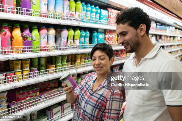 young couple reading the label off of dairy product at the refrigerated section of the supermarket both smiling - dairy aisle stock pictures, royalty-free photos & images