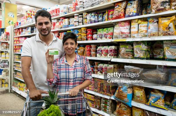 couple at the supermarket holding a loyalty card facing camera smiling - loyalty card stock pictures, royalty-free photos & images