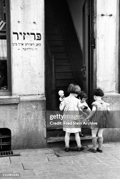 Three girls stand in an open doorway of a building in the Jewish quarter, Antwerp, Belgium, 1937.