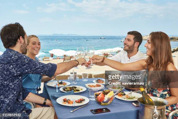 parejas jóvenes tostando durante el almuerzo en sunny costa brava cafe - friends sharing mediterranean fotografías e imágenes de stock