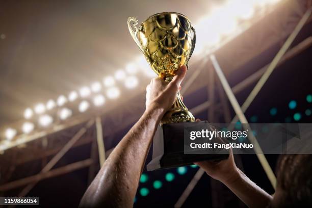 atleta che tiene la coppa dei trofei sopra la testa nello stadio - trofeo foto e immagini stock