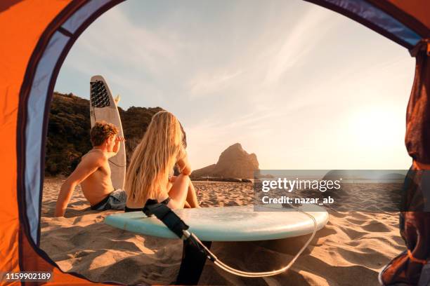view of surfers from tent enjoying sunset at beach. - summer camping new zealand stock pictures, royalty-free photos & images