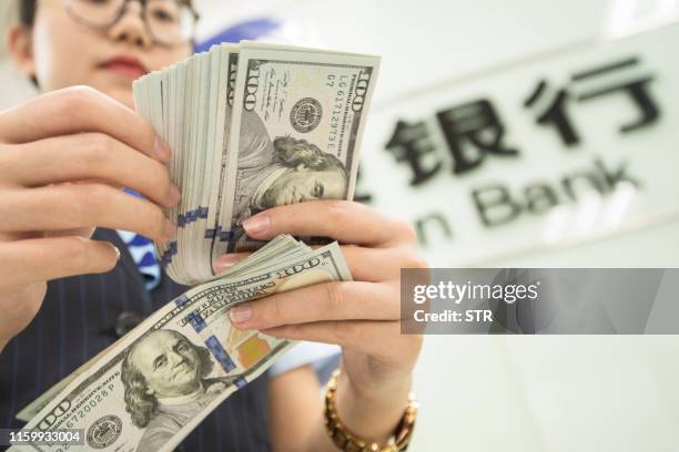 Chinese bank employee counts US dollar bills at a bank counter in Nantong in China's eastern Jiangsu province on August 6, 2019. - The Chinese...