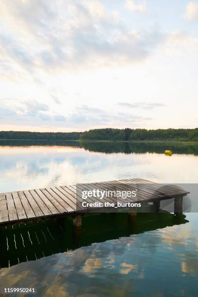 jetty at idyllic lake during sunset, clouds are reflected in the water - ponton bois photos et images de collection