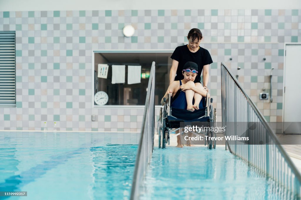 Paraplegic woman in a wheelchair and her coach entering or leaving the pool before or after training for competitive swimming