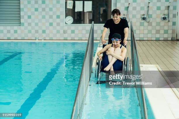 Paraplegic woman in a wheelchair and her coach entering or leaving the pool before or after training for competitive swimming