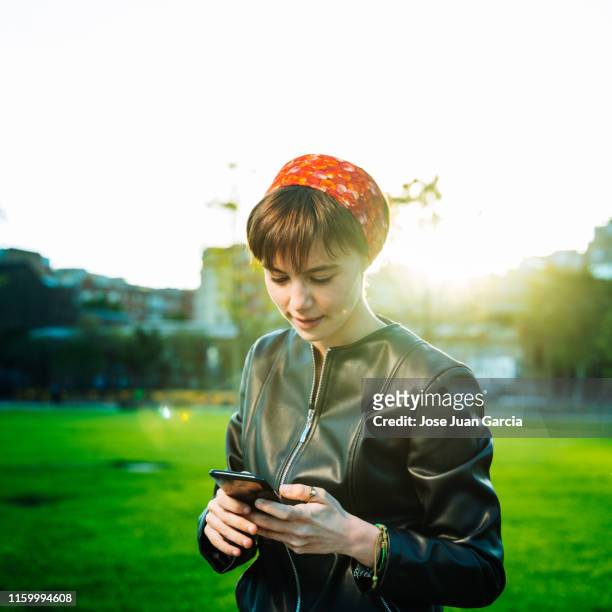 cheerful young woman using phone in a park - western europe stock pictures, royalty-free photos & images