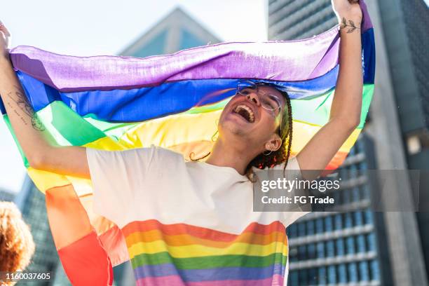glücklicher mann feiert mit regenbogenfahne während der lgbtqi-parade in sao paulo - regenbogenfahne stock-fotos und bilder