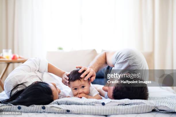 affectionate young couple in love with a baby at home, resting on bed. - family time stock pictures, royalty-free photos & images
