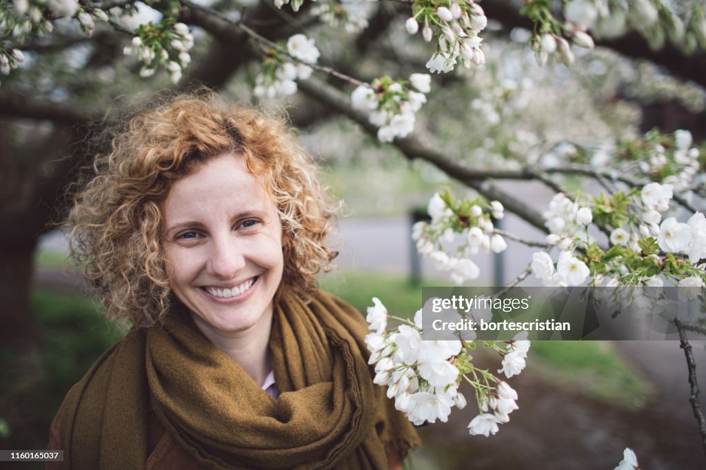 Portrait Of Smiling Woman With Curly Hair By Flowering Tree