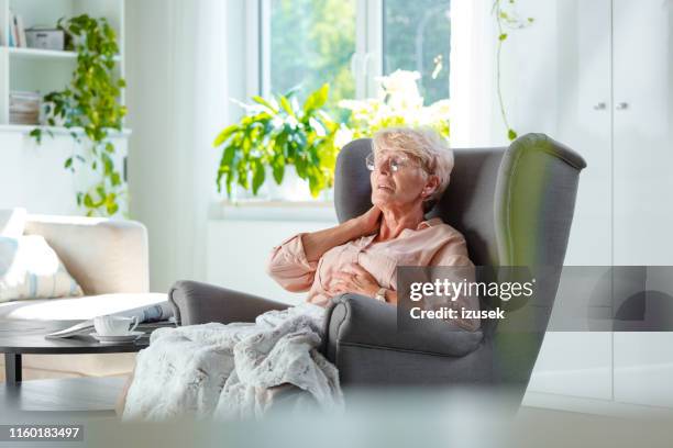 首の痛みに苦しむ高齢女性 - 肘掛け椅子 ストッ�クフォトと画像