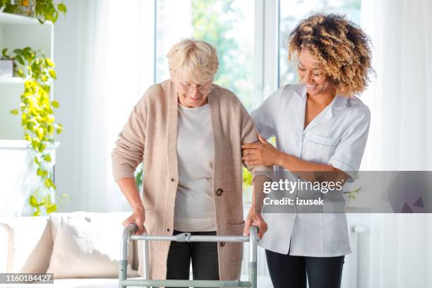 vrolijke vriendelijke verpleegkundige helpen oudere vrouw - looprek stockfoto's en -beelden