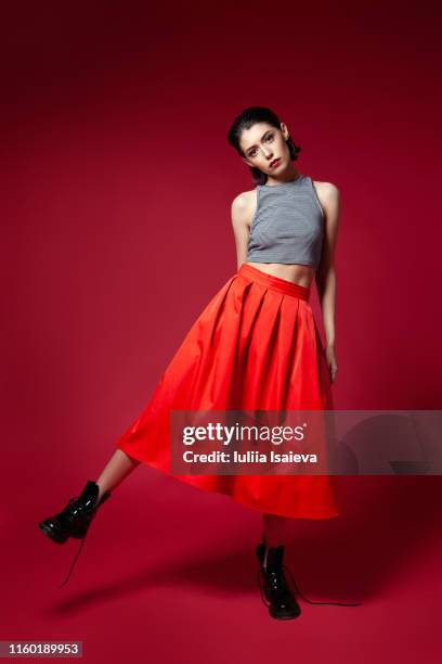 skinny young woman in red skirt posing in studio - portrait femme fond rouge adulte photos et images de collection