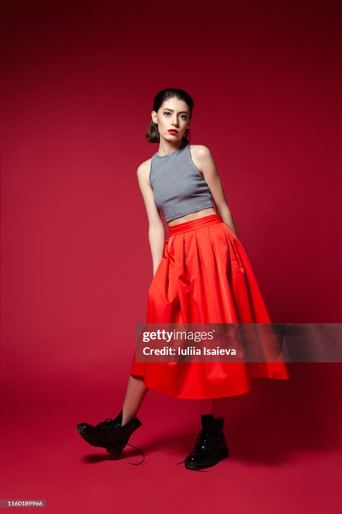 Skinny young woman in red skirt posing in studio