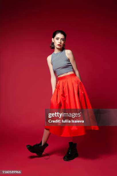 skinny young woman in red skirt posing in studio - portrait femme fond rouge adulte photos et images de collection