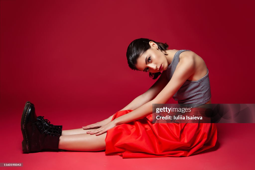 Slender stylish female sitting on red background