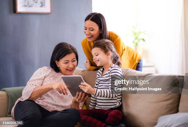 grandmother, mother and granddaughter sitting on sofa at home, using tablet computer. - granny flat stock pictures, royalty-free photos & images