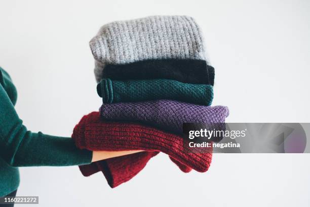 young woman in green sweater stand on the side holding stack of five different knitted warm winter sweaters - warme kleding stockfoto's en -beelden