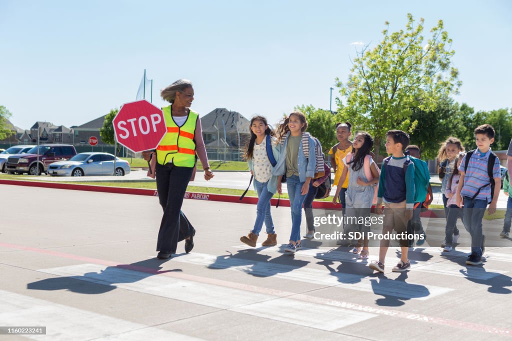 Female crossing guard helping schoolchildren cross street