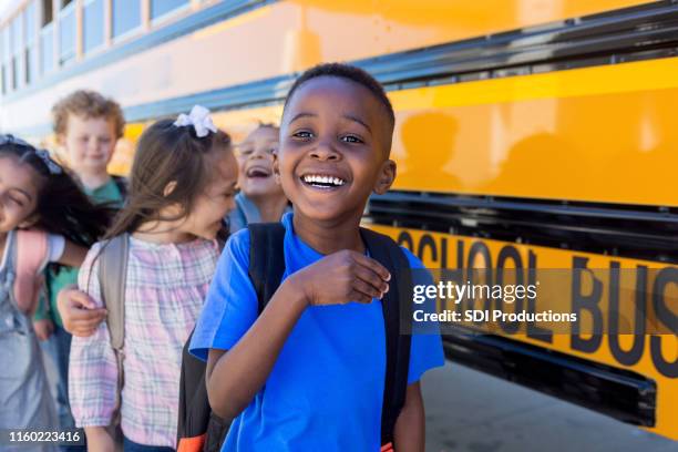 elementary school children goof off and laugh by bus - child rucksack stock pictures, royalty-free photos & images