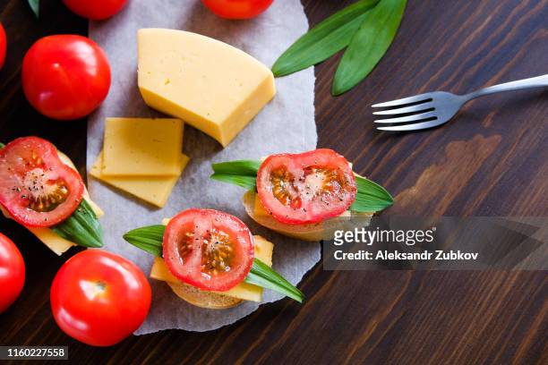 slices of bread, sandwiches, knife, cutting board, red tomatoes, salt shaker, cheese, greens on a wooden table, close-up. the concept of cooking breakfast or snacks, organic farm products. home life. - image teintée photos et images de collection