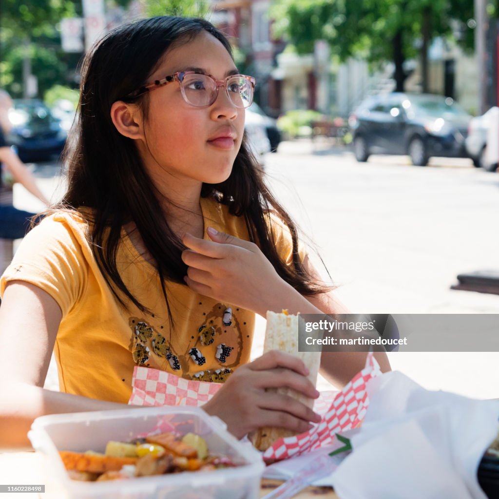 Teenage girl eating take out food outdoors in city.