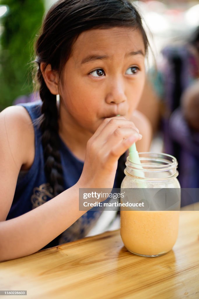 Teenage girl drinking smoothie in reusable jar with reusable straw.