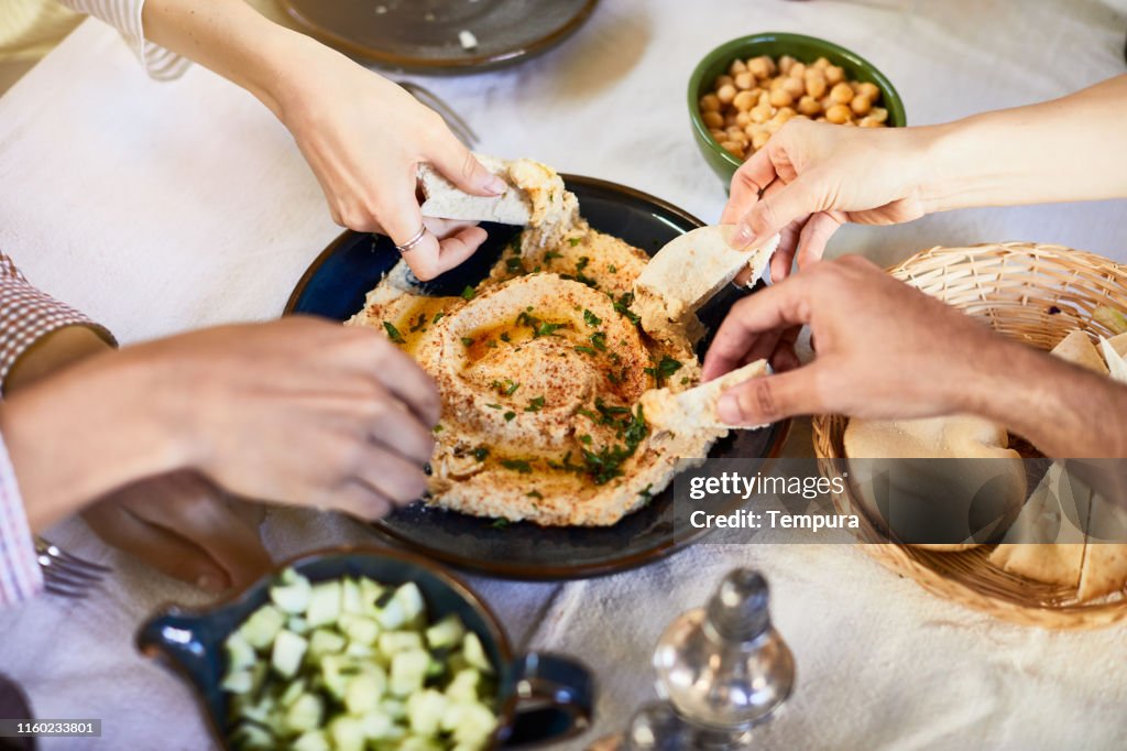 Vegan food, hands dipping hummus.
