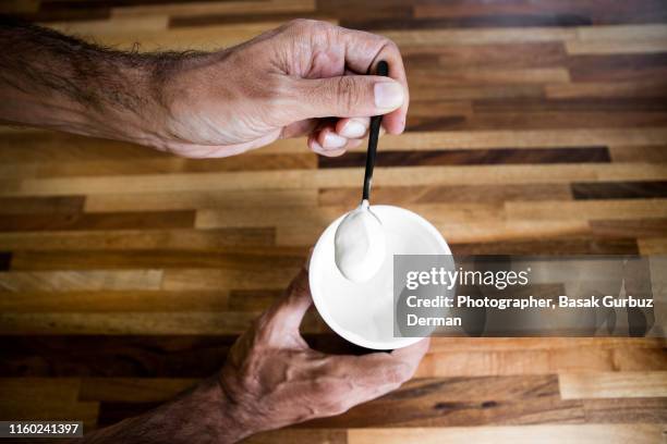 a man holding a black spoon full of creamy yogurt, wooden table on the background - yogurt spoon stock-fotos und bilder