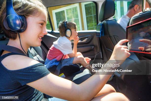 preteen girl and younger brother using tablet inside car during a road trip - girl in car with ipad stock pictures, royalty-free photos & images