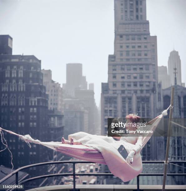 Dancer and singer Gwen Verdon is lying in a hammock over looking NYC holding her hand up, dressed in a gown.