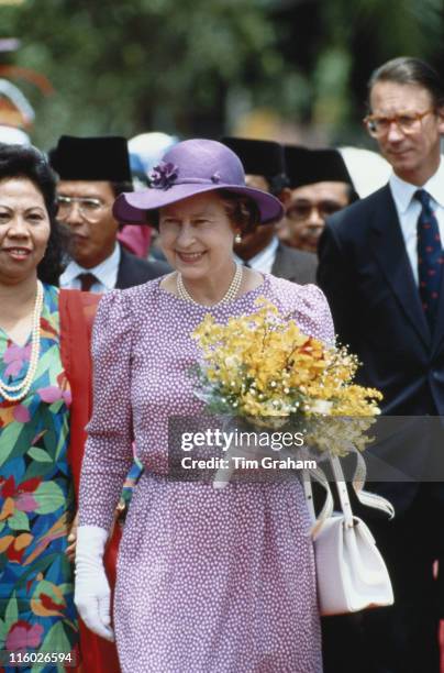 Queen Elizabeth II, carrying a small bouquet of flowers, and her Private Secretary, Sir Robert Fellowes during a state visit to Malaysia, in October...