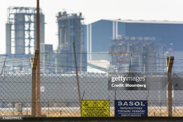 Warning signs in English and Afrikaans language sit on a security fence along the perimeter of the Sasol Ltd. Sasol One Site in Sasolburg, South...