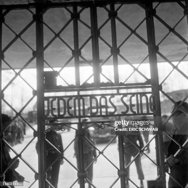 Prisoners and US army soldiers stand behind the gate of Buchenwald concentration camp on which it is written "Jedem das seine" in April 1945. -...