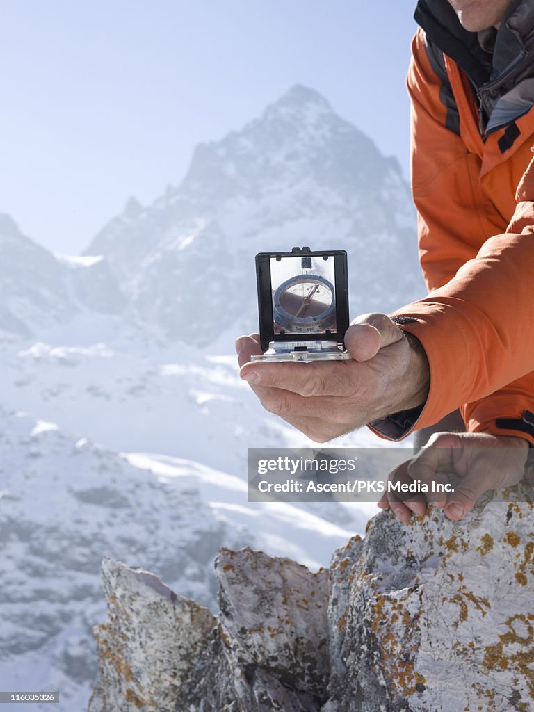 Mountaineer holds compass pointed towards peak