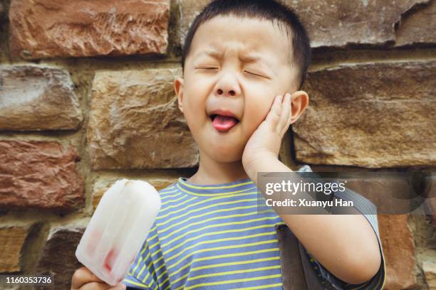 cute little boy standing eating popsicle, toothache - tandpijn stockfoto's en -beelden