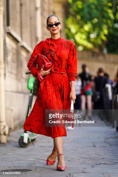 Lana El Sahely wears sunglasses, a red floral print pleated dress, a red bag, red shoes, outside Valentino, during Paris Fashion Week -Haute Couture...