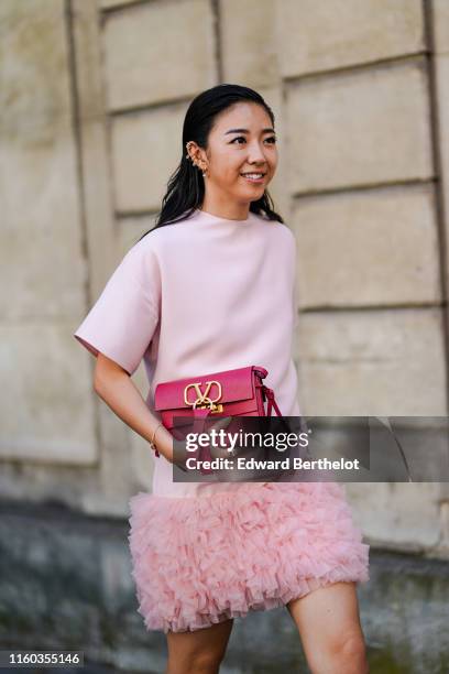 Yuwei Zhangzou wears a pink dress with fluffy part, a red Valentino bag with logo, outside Valentino, during Paris Fashion Week -Haute Couture...