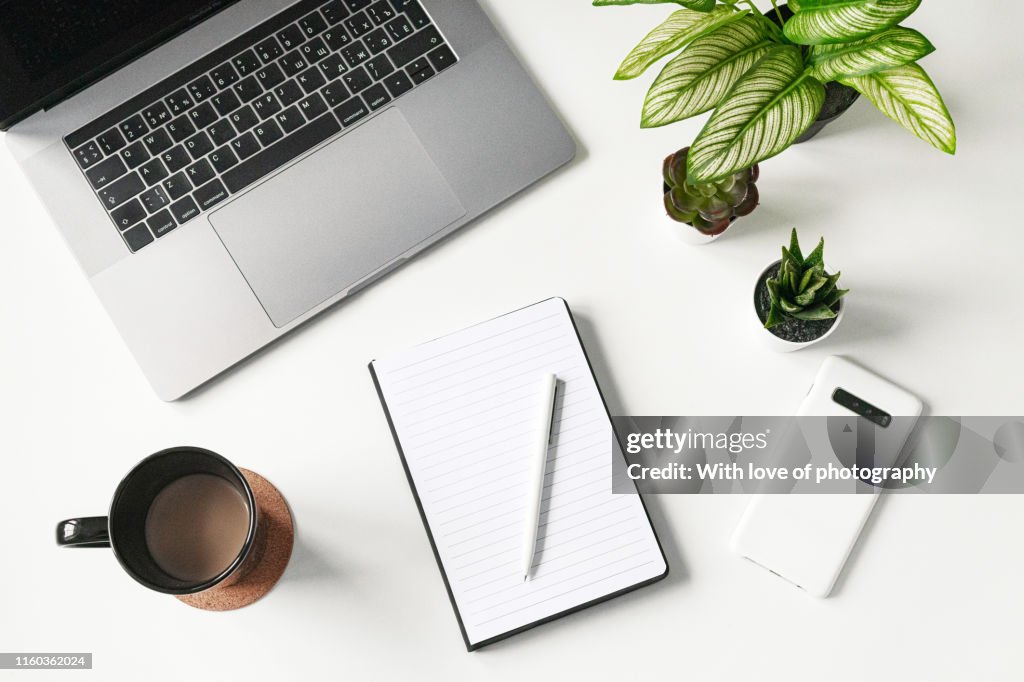 Modern white office desk table with laptop, smartphone and blank notebook and cup of coffee, flatlay, top view workspace, business