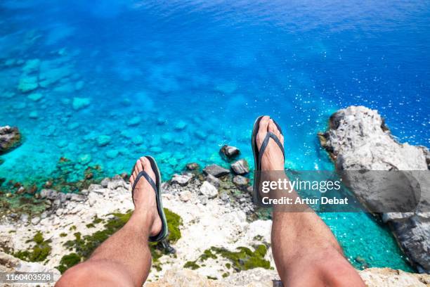 hanging feet from the stunning coastline from the edge of the beautiful zakynthos island in greece. - thong stock pictures, royalty-free photos & images