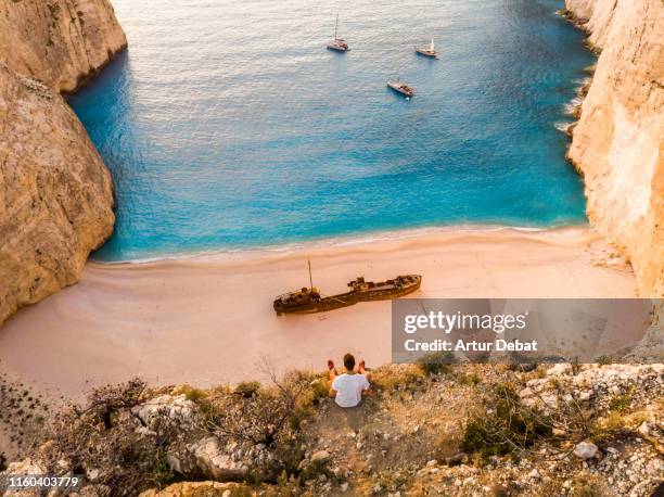 aerial view of guy from viewpoint watching the famous shipwreck beach in greece. - sunset zacinto foto e immagini stock