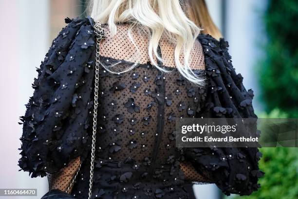 Guest wears a black puff sleeves dress with black fabric flowers embroideries, outside the "Scandal A Paris" : Jean-Paul Gaultier's New Fragance...