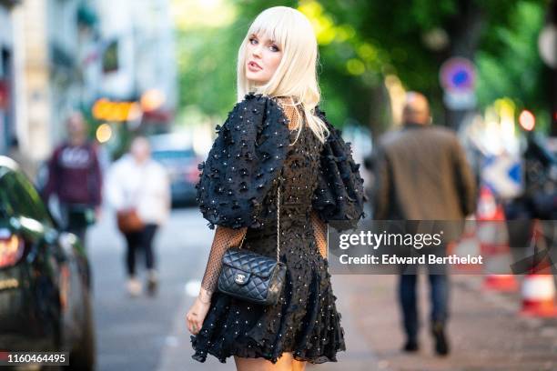 Bonnie Strange wears a black puff sleeves dress with black fabric flowers embroideries, a black Chanel bag, outside the "Scandal A Paris" : Jean-Paul...