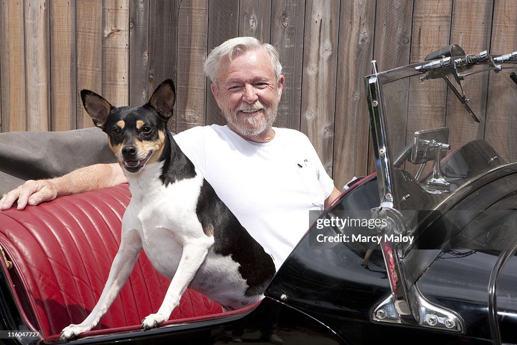 Older man sitting in a classic car with small dog.