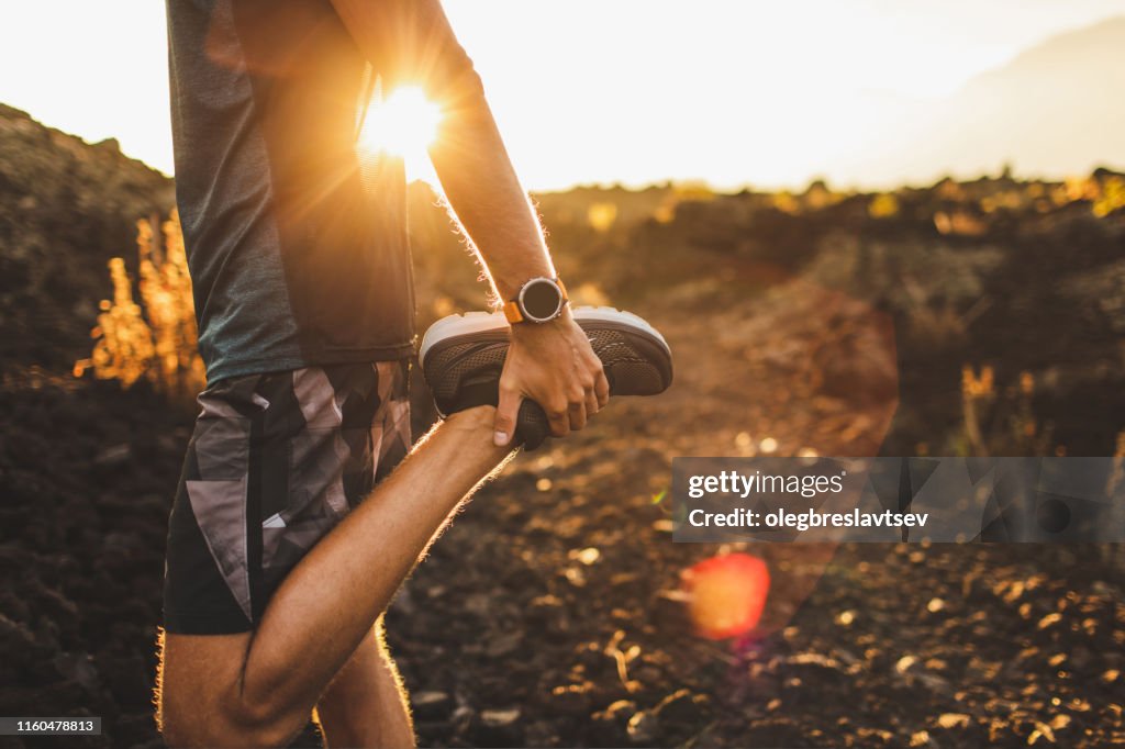 Man runner stretching been en voeten en de voorbereiding voor het runnen van buiten. Smart Watch of fitness tracker bij de hand. Mooie zon licht op de achtergrond. Actief en gezond lifestyle concept.