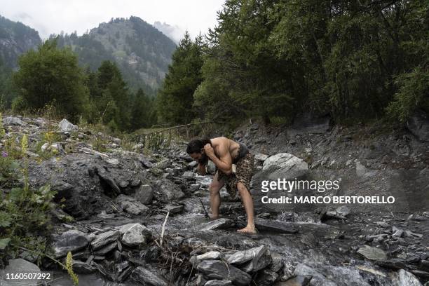 Guido Camia dressed as a Neanderthal Cave man washes himself in a river in Chianale, in the Italian Alps, near the French border, on August 7, 2019....