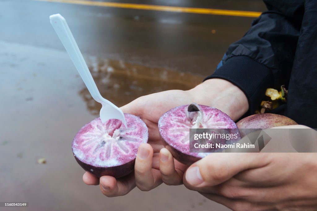 Man holding Star Apple fruit from a road-side stall in Hawaii