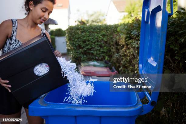 young woman emptying shredded paper into a yard recycling bin - mixed recycling bin stock pictures, royalty-free photos & images