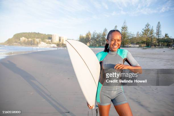 young indigenous australian girl on the beach in a wetsuit with her surfboard - surfer australia stock-fotos und bilder