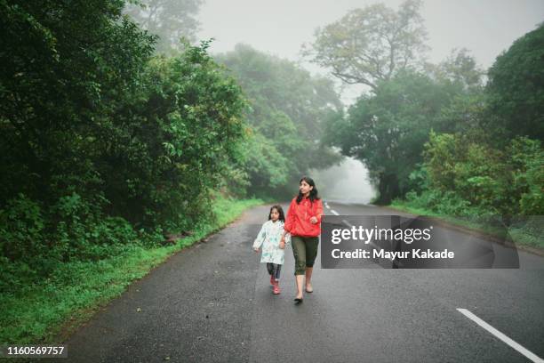 mère et fille marchant sur la route pendant la saison de la mousson - vêtement de pluie photos et images de collection